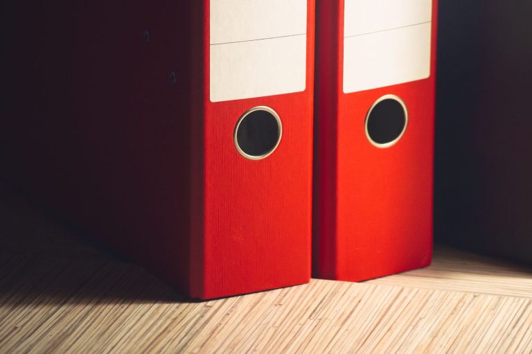 Two red lever arch binders on a wooden desk